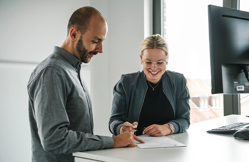 Zwei Mitarbeitende der Kanzlei Runde Glüsing Baune besprechen gemeinsam ein Dokument zur Finanz- oder Lohnbuchhaltung am Steharbeitsplatz