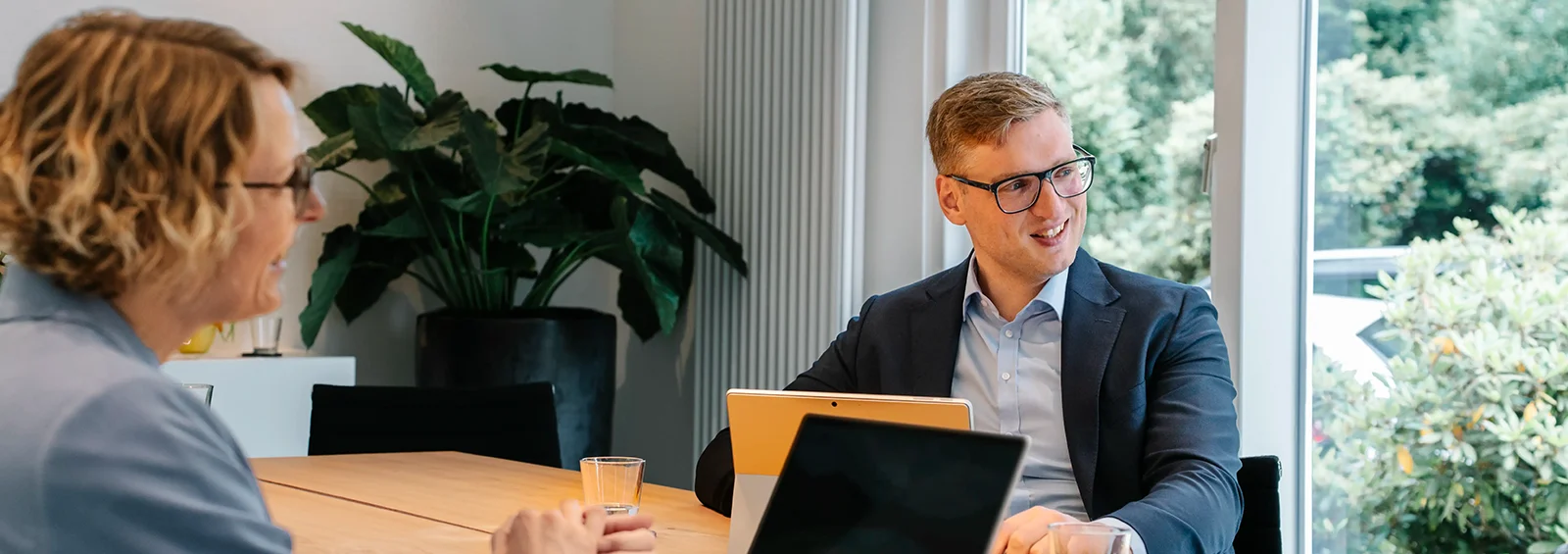 Mitarbeitende der Steuerkanzlei Runde Glüsing Baune im Gespräch an einem großen Holztisch mit Laptops und Getränken im modernen Besprechungsraum in Ibbenbüren
